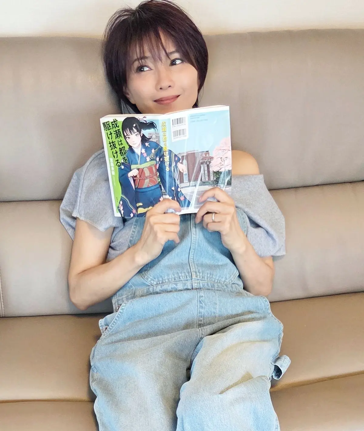女性がソファに座り、漫画を読みながら微笑んでいる。漫画の表紙には着物姿の女性が描かれている。