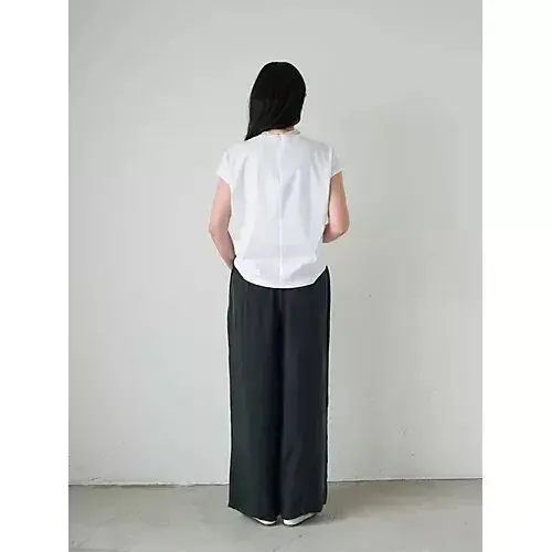 白い半袖トップスとグレーのワイドパンツを着た女性の後ろ姿、壁に映る影