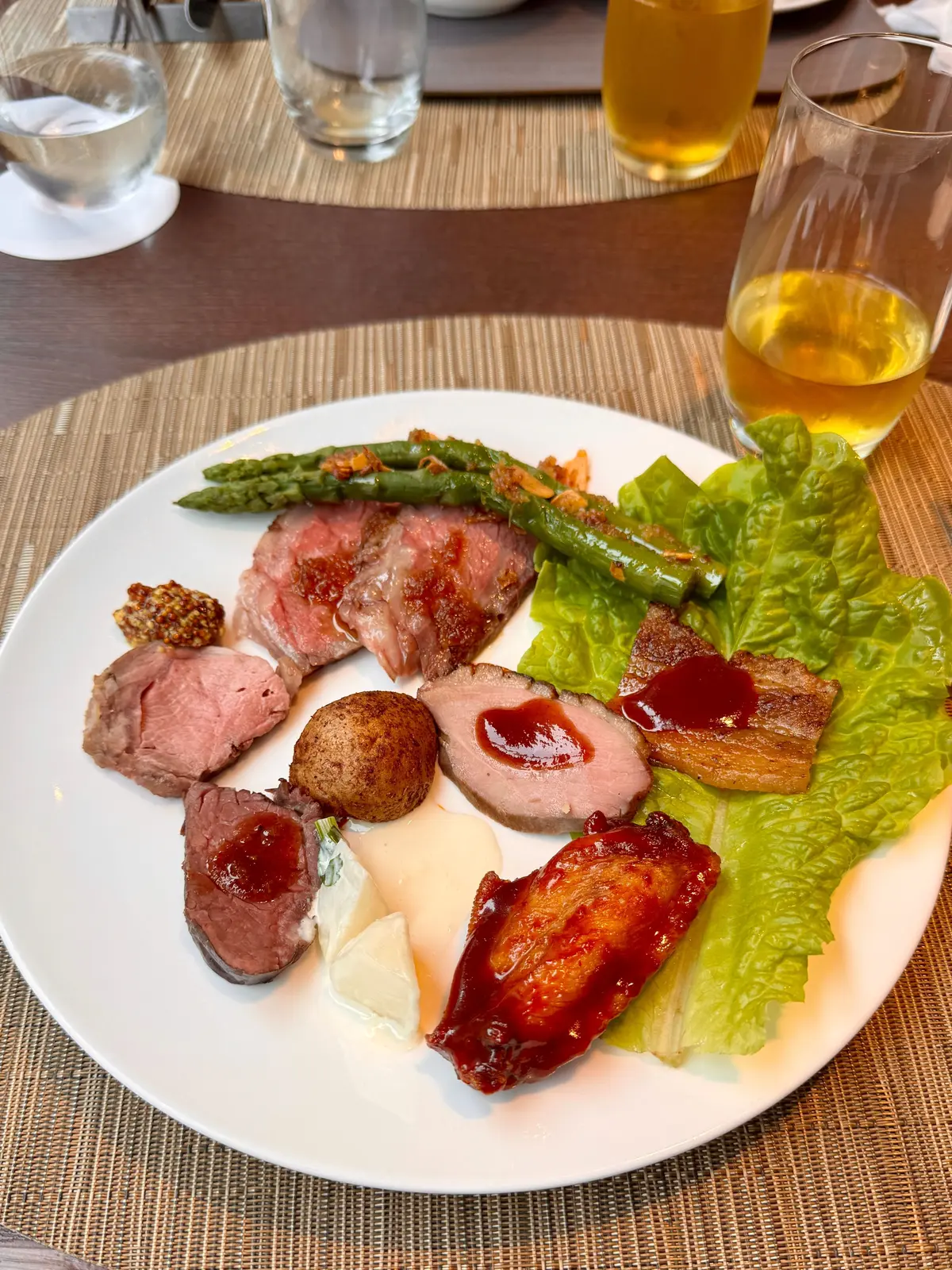白いプレートにアスパラガス、肉、ポテト、チーズ、トマトソースが盛り付けられ、背景にビールと水のグラスが置かれている