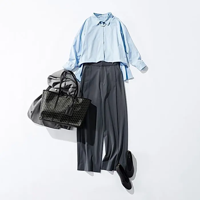 白背景に、ブルーのシャツ、グレーのワイドパンツ、黒いパンプス、黒いバッグが置かれている。シャツはボタンを開け、襟元にアクセサリーがある。バッグは柄が入り、中にグレーの布が包まれている。