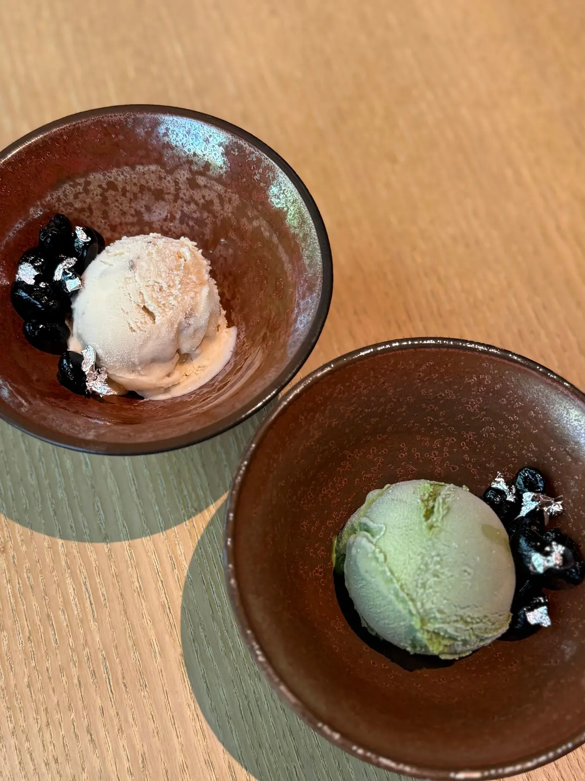 茶色の器に盛り付けられた、ピンク色と緑色のシャーベット。器の周りには黒いゼリーと金色の葉が散らされている。
