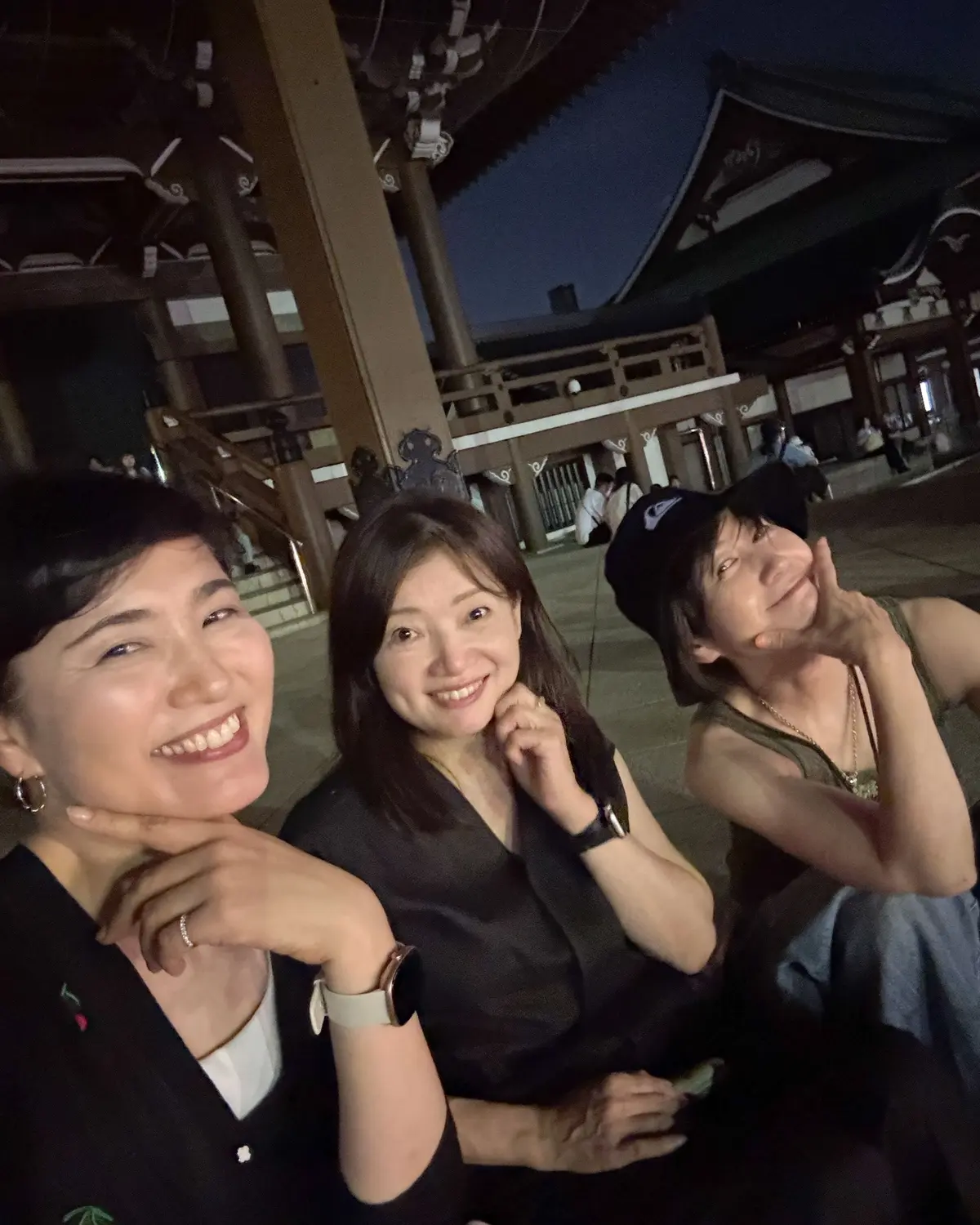 夜の寺院を背景に、3人の女性が笑顔で写っている。左から2人目は真ん中に位置し、他の2人はそれぞれ左右にいる。全員がカメラに向かってポーズをとっている。