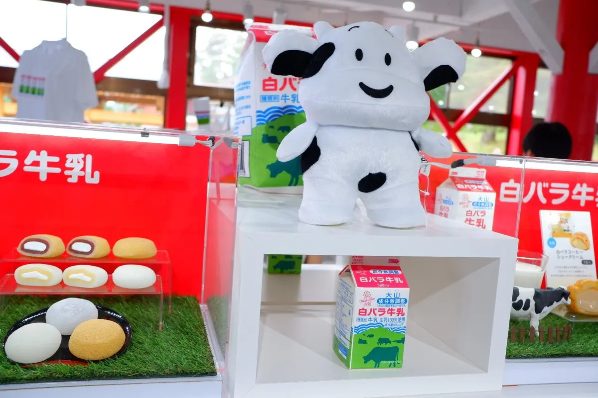 白い牛のぬいぐるみと白バラ牛乳の箱、チーズ、卵などが並んだ展示台