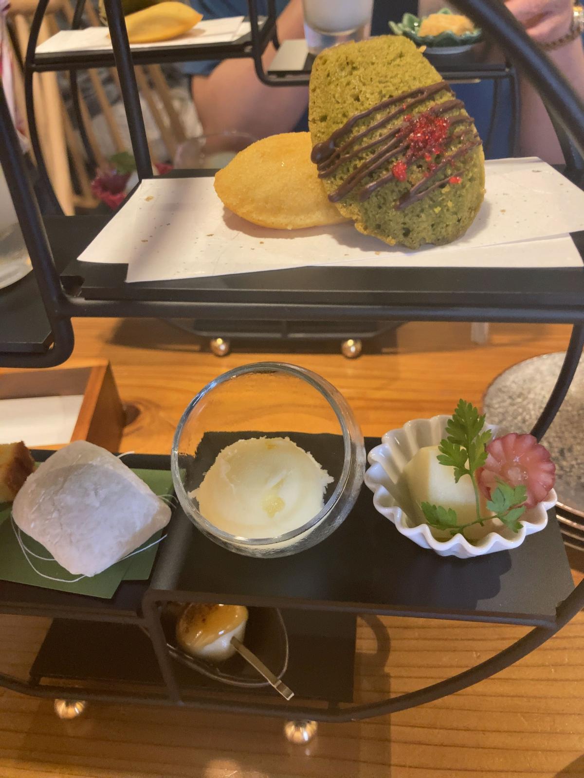 緑茶と黄色のクッキーにチョコレートと赤い装飾がのった二つのクッキーと、クリームとパセリを添えたデザートが並ぶティーセット