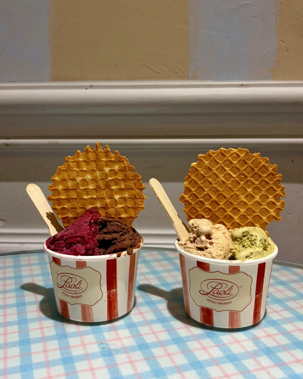 赤と緑のアイスクリームが2つのカップに盛り付けられ、両方ともワッフルがトッピングされています。左のカップには赤と黒のアイスクリーム、右のカップには緑とベージュのアイスクリームが入っています。