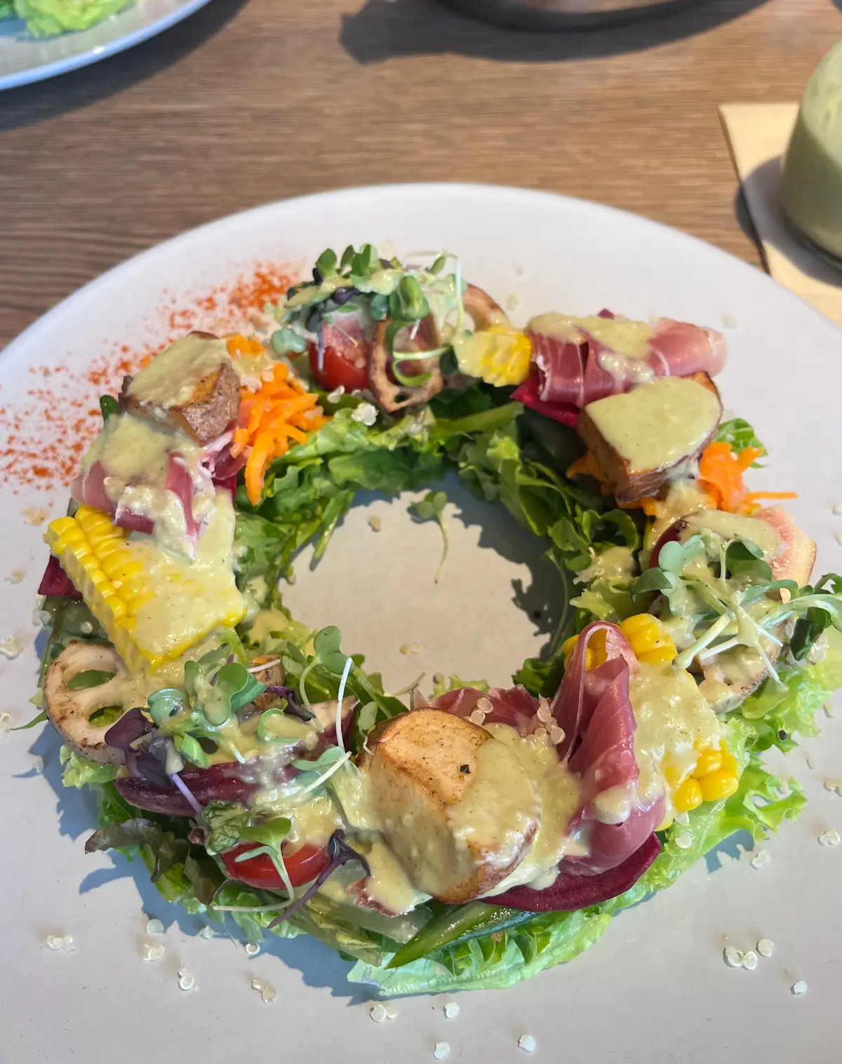 白い皿に盛り付けられた、緑色の葉野菜をベースにしたサラダ。中心に赤紫色のビーツ、黄色いとうもろこし、茶色の肉、緑色のソースが配置され、マイクログリーンとオレンジ色の細切り野菜が添えられている。