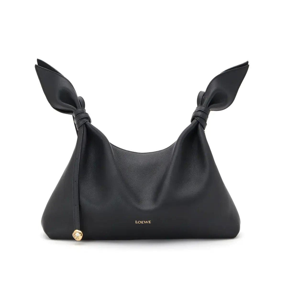 黒のレザー製ハンドバッグで、両側にリボンが付いたデザイン。ブランド名「LOEWE」が刻まれ、金のチャームが付いている。