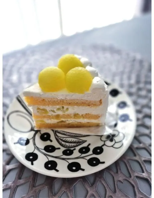 レモンの丸いデコがのった白いクリームとスポンジのレイヤーケーキが、花模様の白い皿に載っている