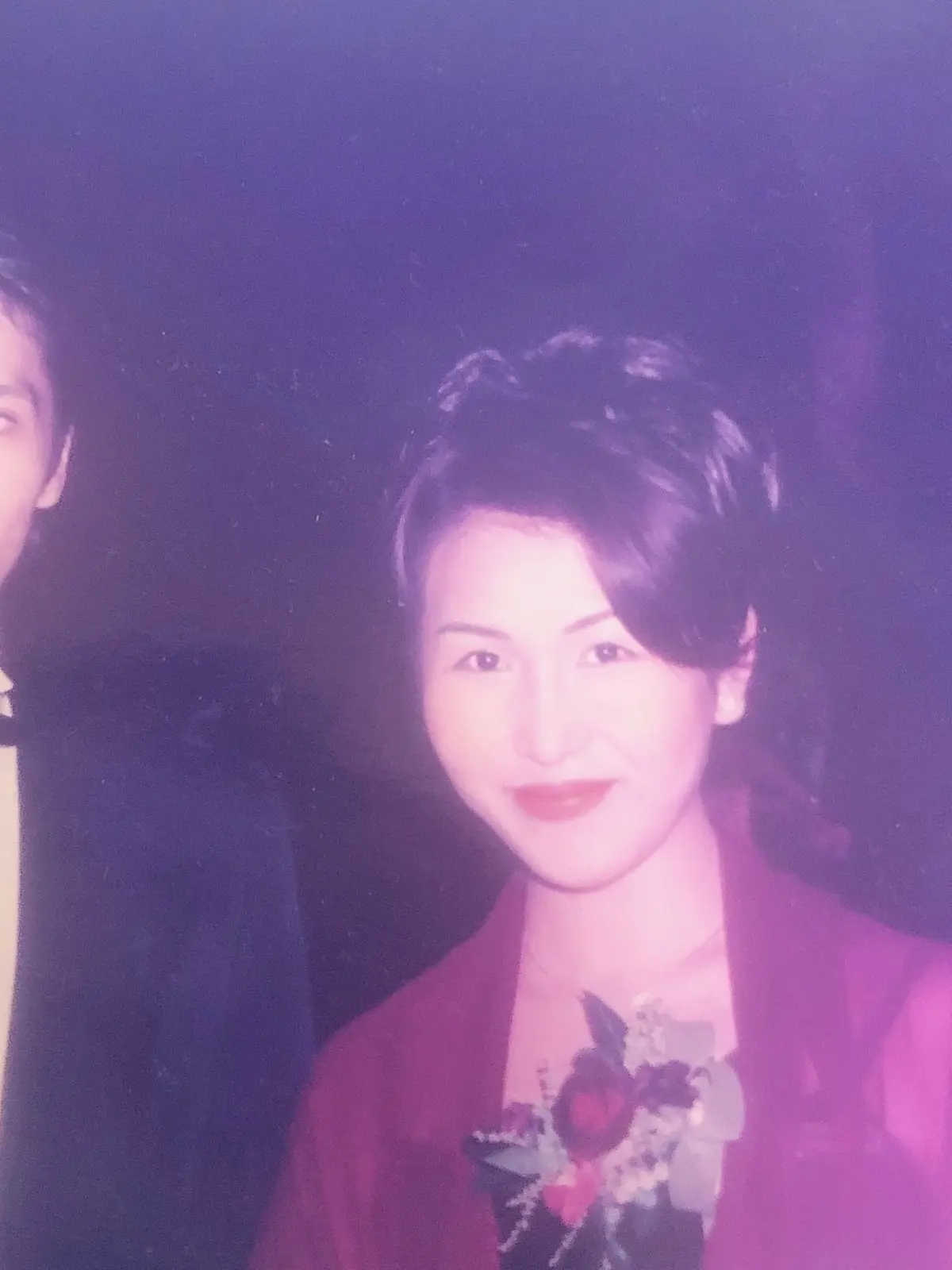 黒のスーツに蝶ネクタイをつけた男性と、赤い着物にピンクのショールを羽織った女性が並んで立っている写真。背景は暗く、人物は中央に配置されている。