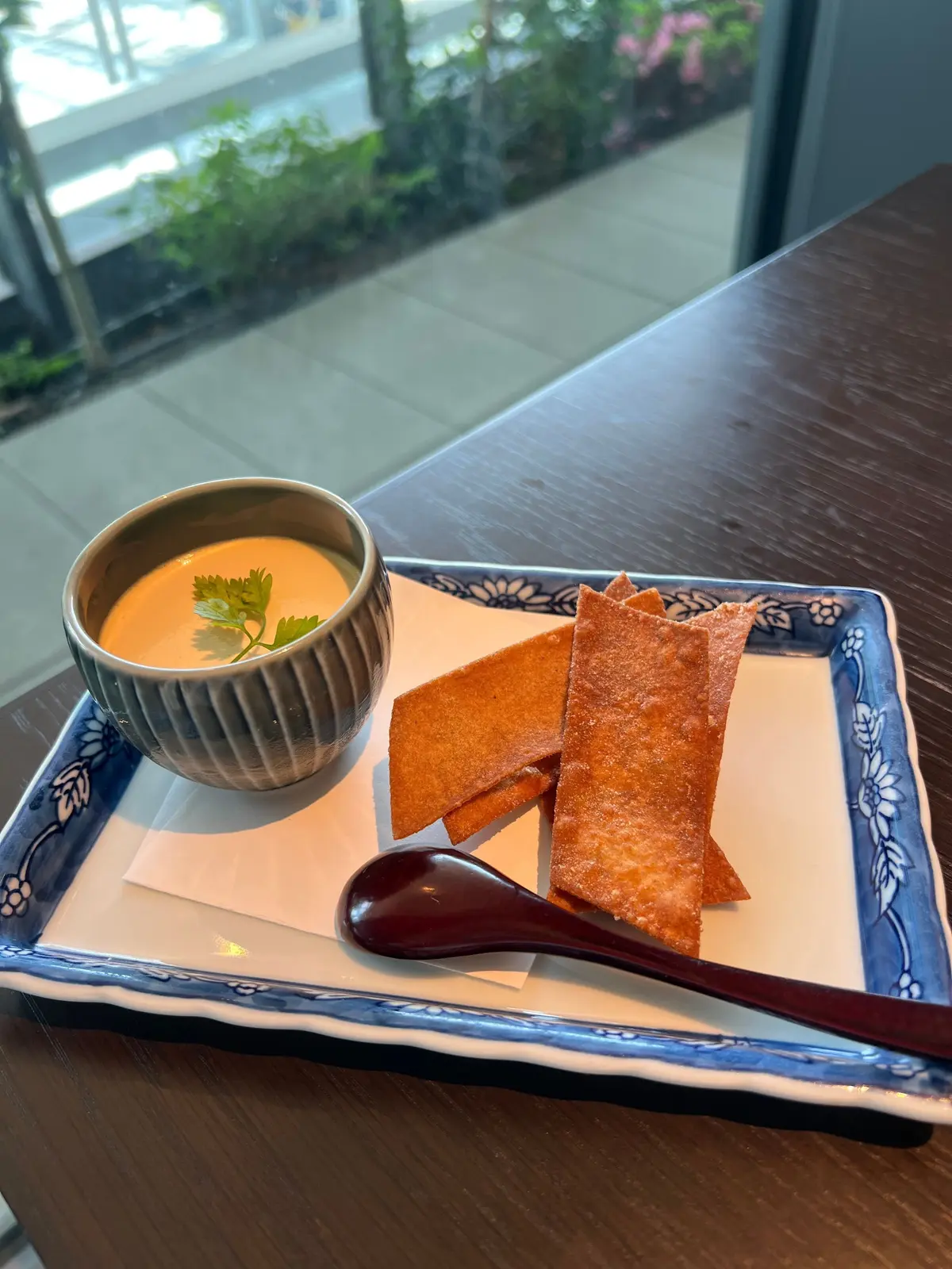 青い花模様のプレートに、茶色いスープの入った小鉢、薄い色の焼き菓子、茶色のスプーンが並んでいる