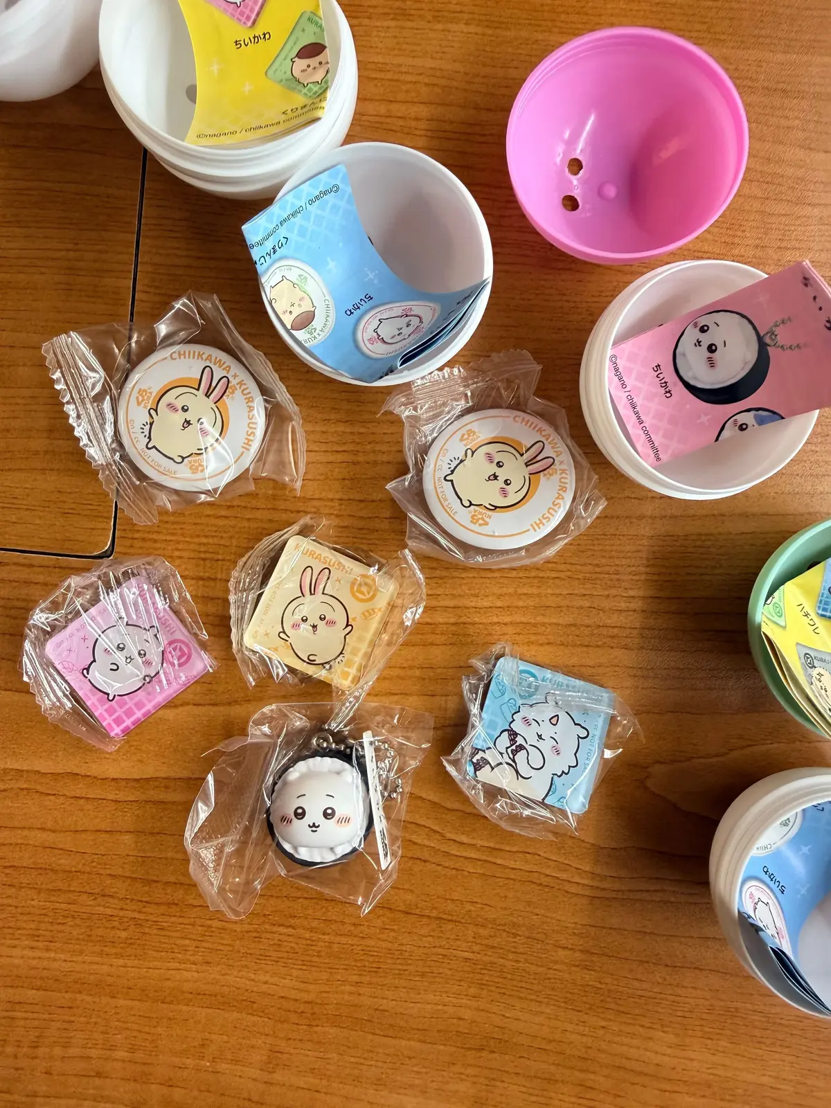木製のテーブルの上に、CHIikawaのグッズが散らばっている様子。白やピンクの小物入れ、キーホルダー、ステッカーなど、様々なアイテムが置かれている。