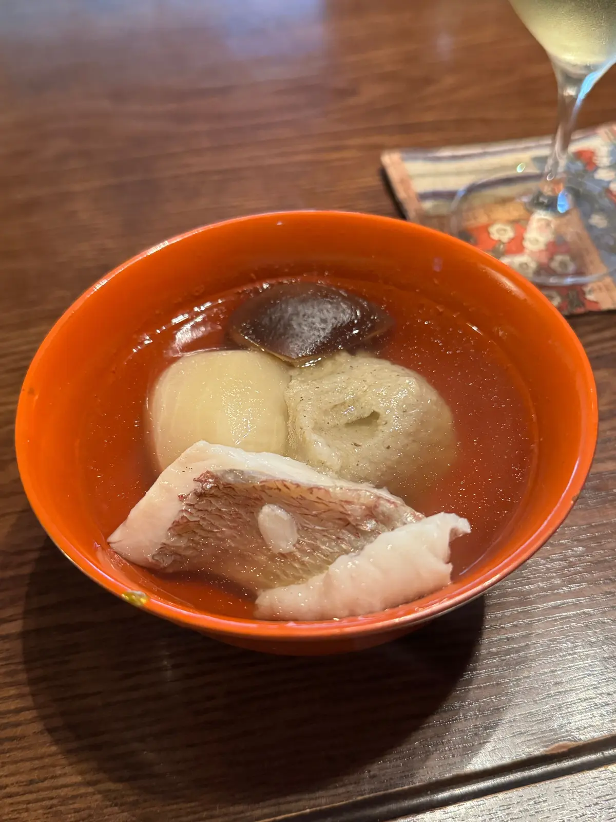 オレンジ色の陶器の椀に入った、薄い茶色のスープ。スープの中には、白い団子、茶色のキノコ、ピンク色の豚肉が浮かんでいる。