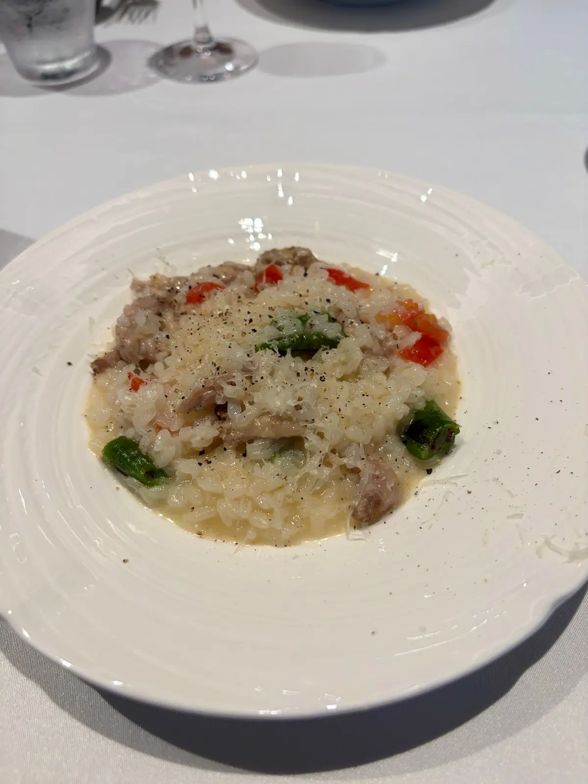 白い皿に盛り付けられた、肉と野菜が乗ったリゾット。リゾットはクリーム状で、黒胡椒がふりかけられている。肉は細かく刻まれ、トマトと緑色の野菜が添えられている。