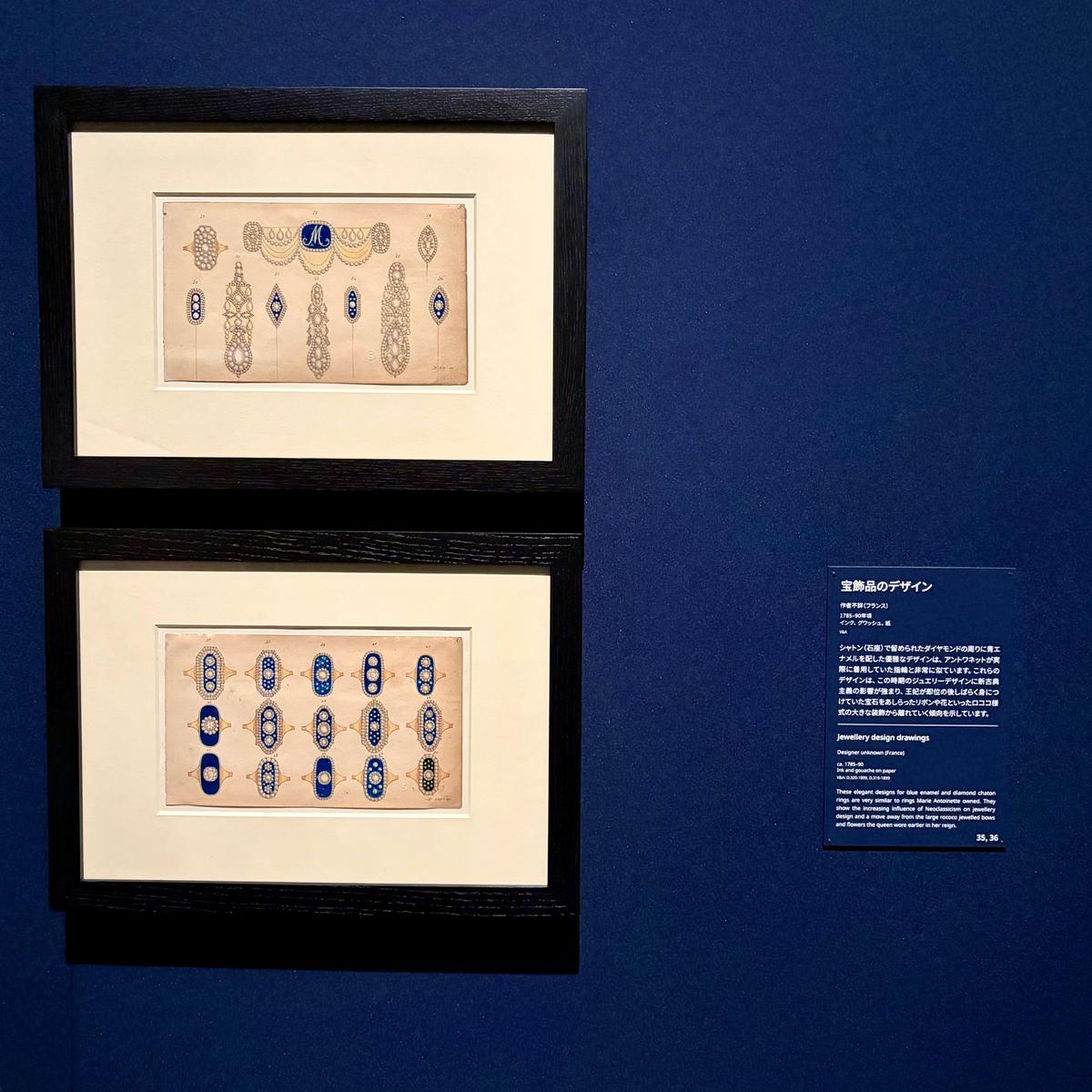 美術館の展示ケースに収められた、2枚のジュエリーデザインの素描。上段は、王冠と花をモチーフにした細長いデザインが複数並んでいる。下段は、幾何学模様と宝石を組み合わせたデザインが並ぶ。背景には日本語の解説文が貼られている。