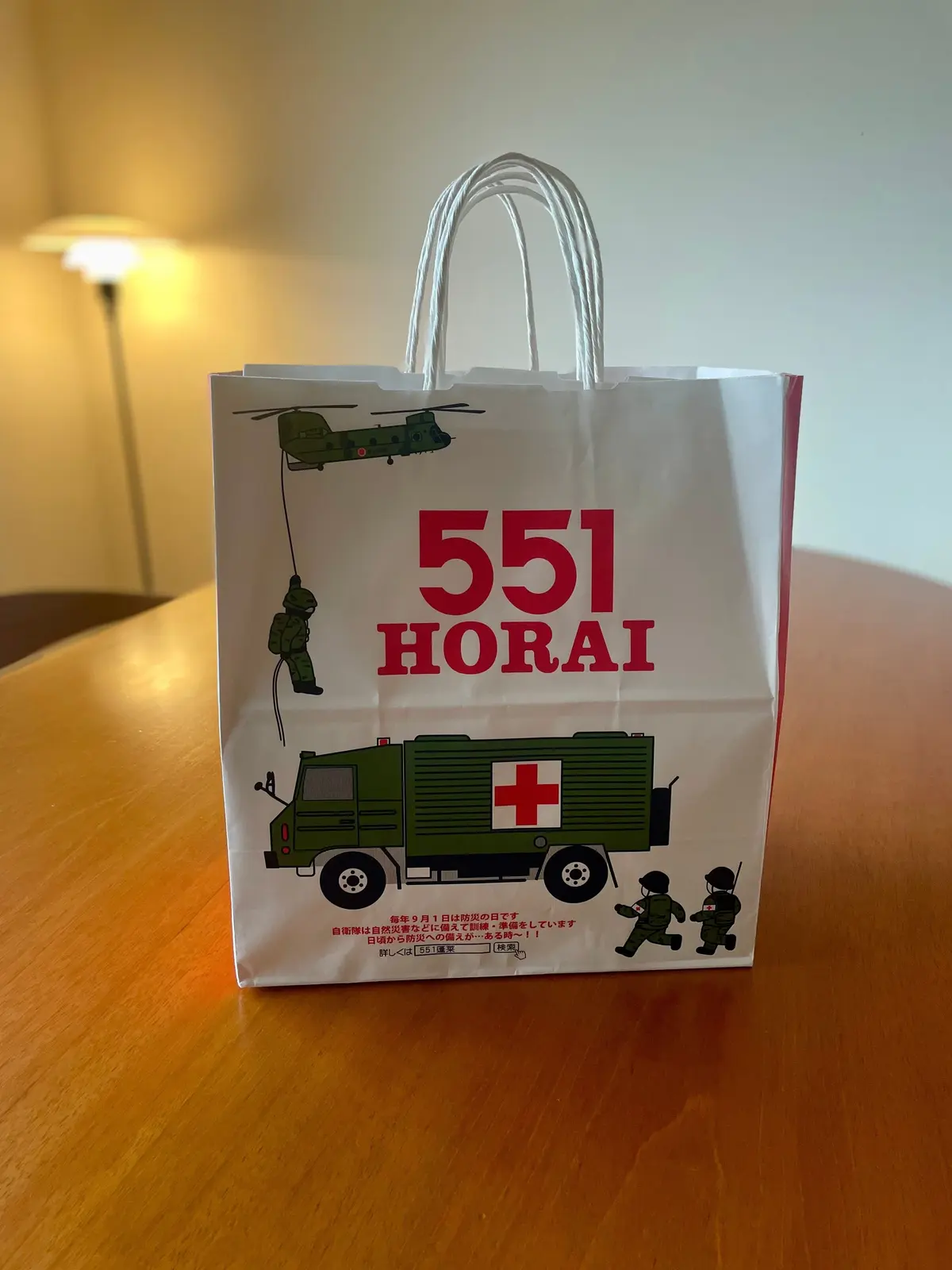 551HORAIのテイクアウト袋。白地に緑色の軍用車両や兵士のイラストが配置。赤色のロゴと文字が目立つ。