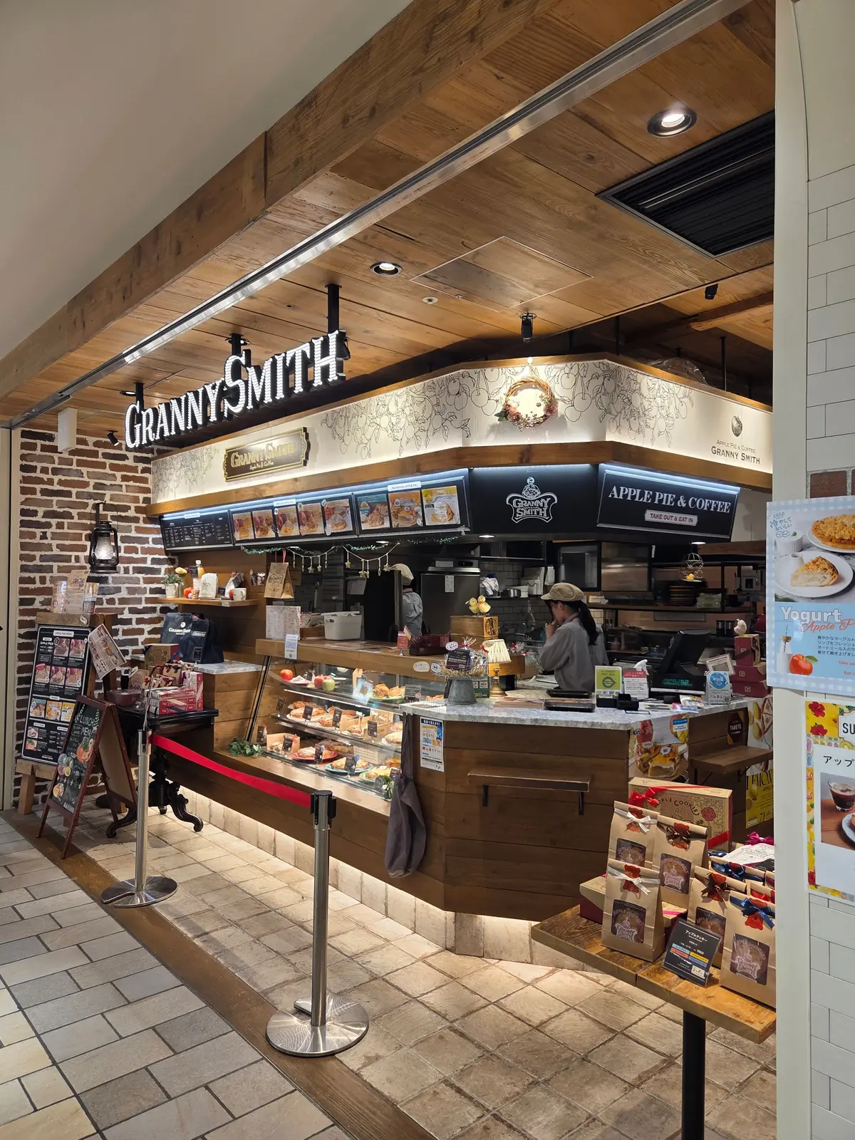 グランニースミス店舗の内部。木目調のカウンターに焼き菓子やドリンクが並び、スタッフが対応している。左壁にはレンガ、右壁は白いタイル。天井は木目調で、ブランドロゴが設置されている。