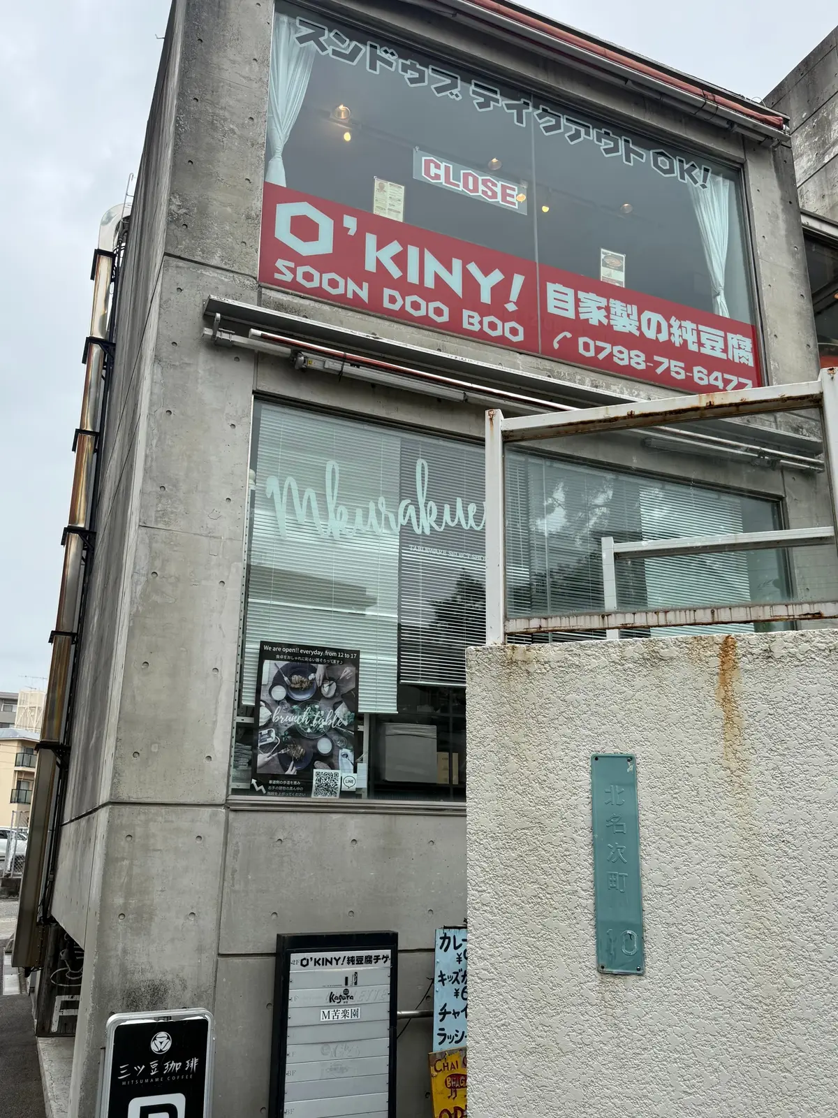 コンクリート造りの2階建て建物。窓に「murasaki」の文字、看板に「O'KINY!」のロゴと「手家製純粋屋」の文字。右下には住所表示のプレート。