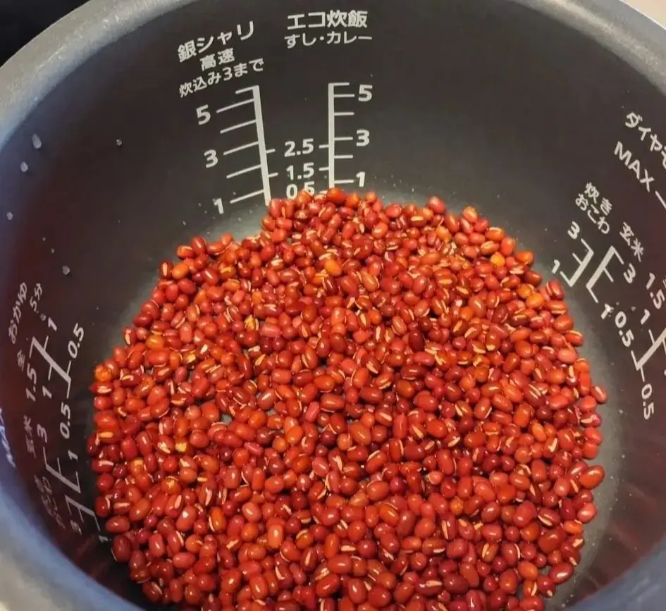 赤褐色の小豆が、計量カップに山のように盛り付けられている。カップ内壁には目盛りが付いており、小豆の量を示すと思われる数字が刻まれている。