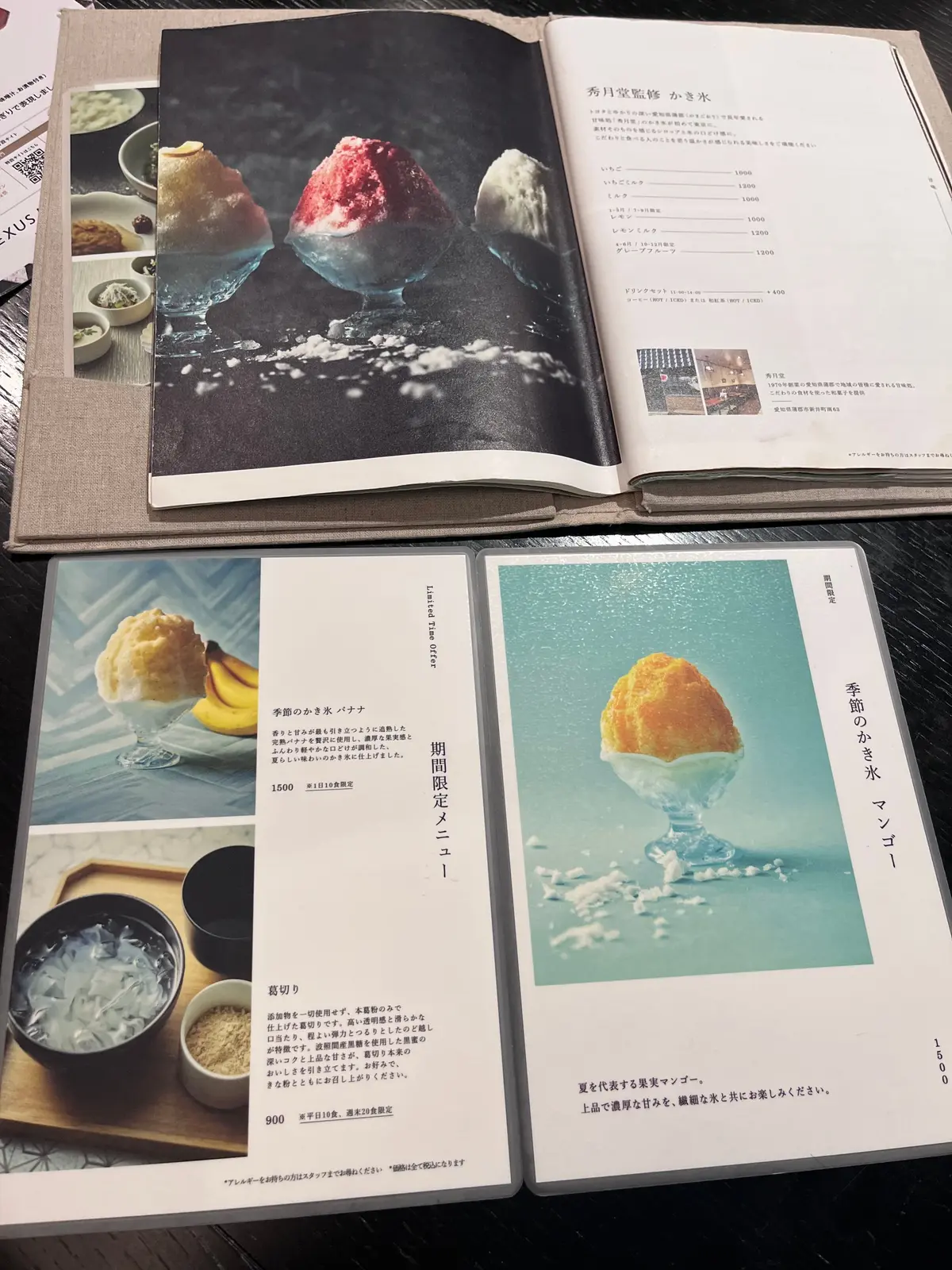 複数の料理写真とメニューが置かれたテーブル。左上には「AUX」と書かれた書籍、右上には「秀司宗堅の小常本」のメニュー、中央には季節限定メニュー、右下には「季箱の小常本 マンゴー」のメニューが置かれている。