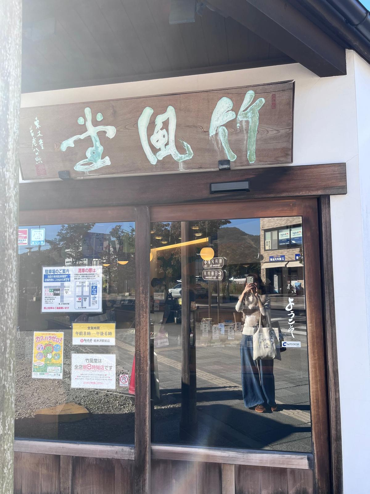 木造の建物に「並岡 Diner」の看板がある。入り口の自動ドアを女性が通ろうとしている。ドアには様々な案内表示が貼られている。背景には駐車場と建物が見える。