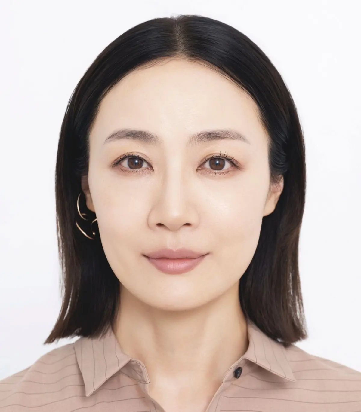 黒髪でショートカットの女性が、淡いピンクの縞模様のシャツを着て、真っ白な背景に正面を向いて映っている。