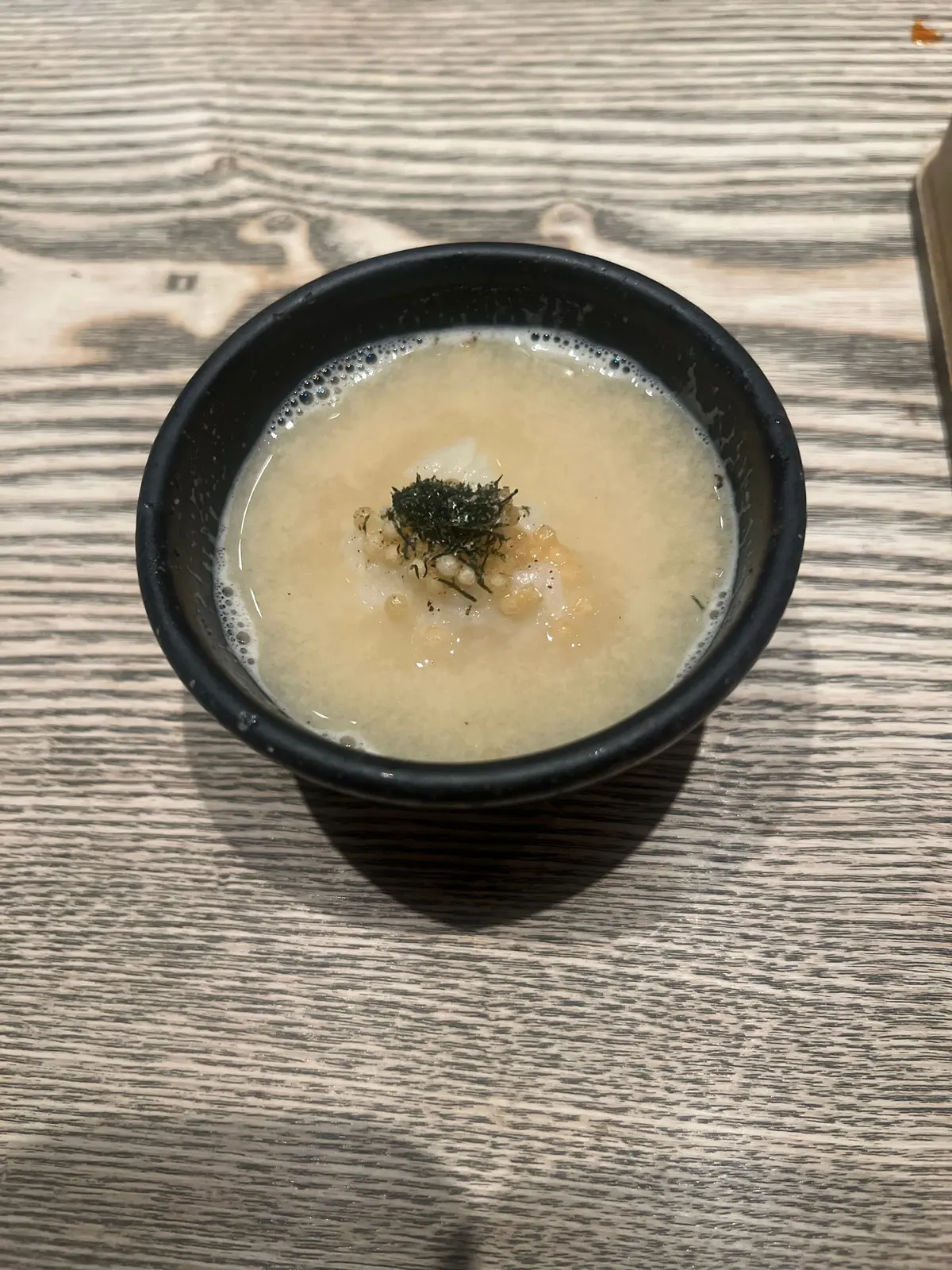 黒い鉢に白いスープ、ワカメと玉ねぎのトッピング