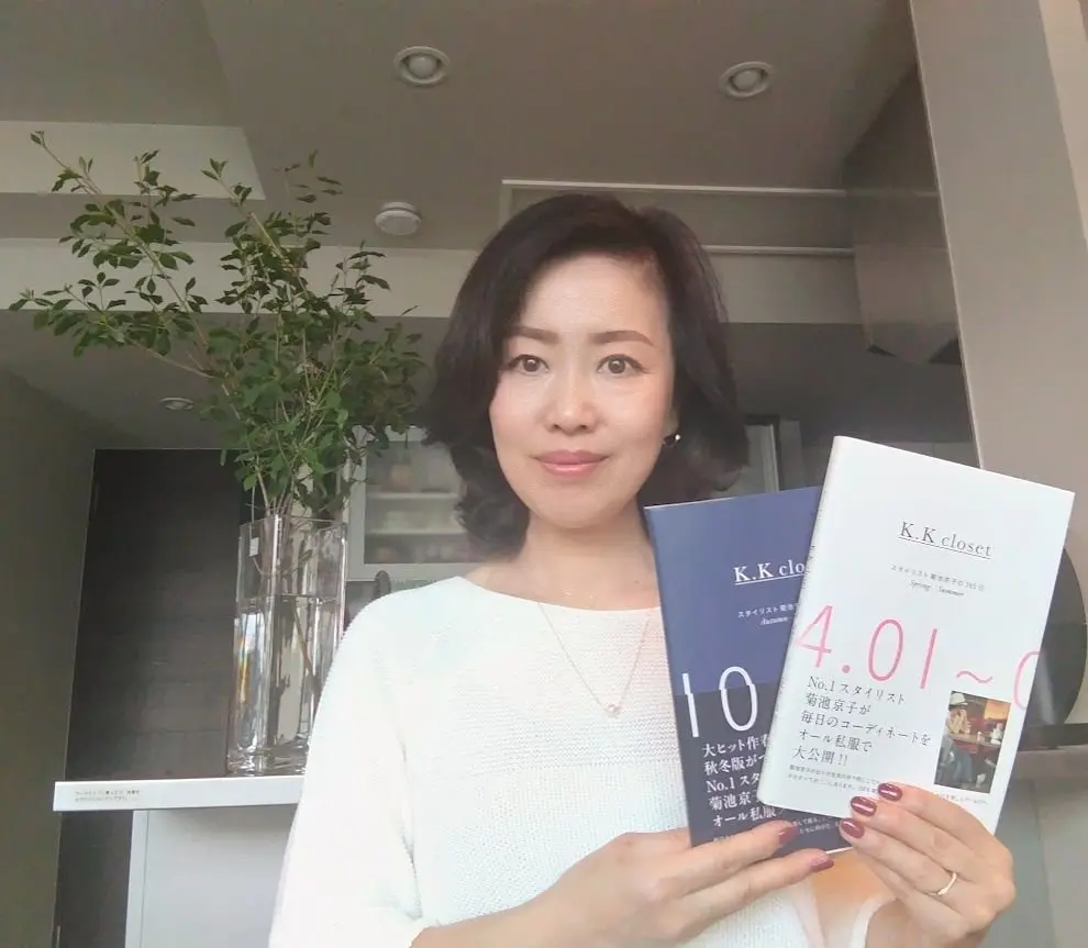 女性が白いセーターを着て、2冊の本を手に持つ。左の本は青い表紙で「401」を大きく表示、右の本は白い表紙で「K.K closet」と書かれている。背景には緑の観葉植物と棚がある。