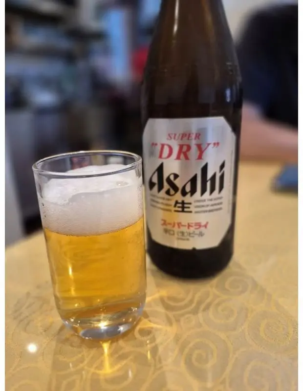Asahi Super Dryのビールが、グラスに注がれており、瓶が横に置かれている。泡立ちが良く、金色を帯びた液体が見える。