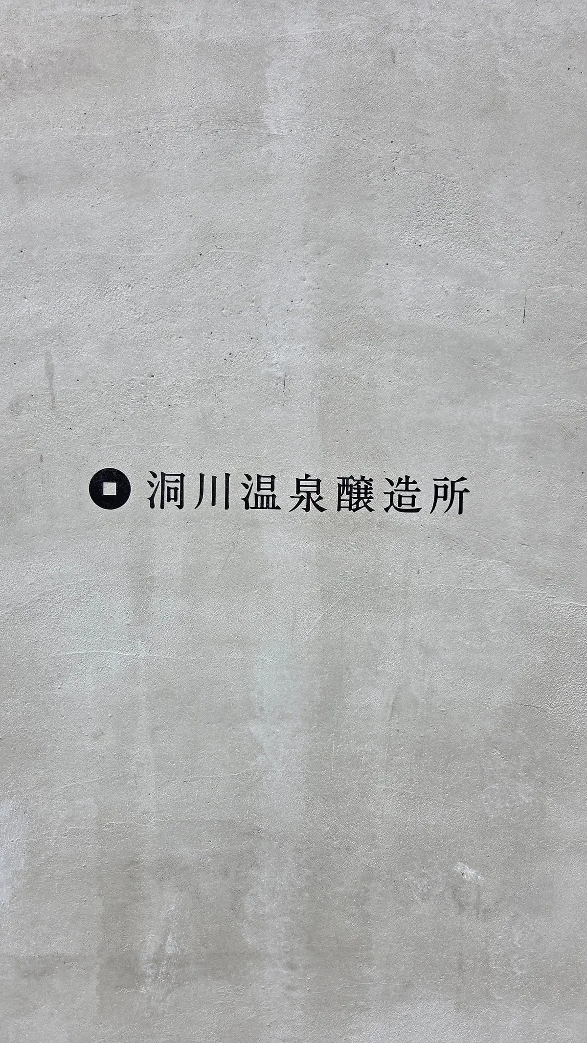 灰色のコンクリート壁に、黒い丸いアイコンと「洞川温泉醸造所」の文字が中央に配置されている。