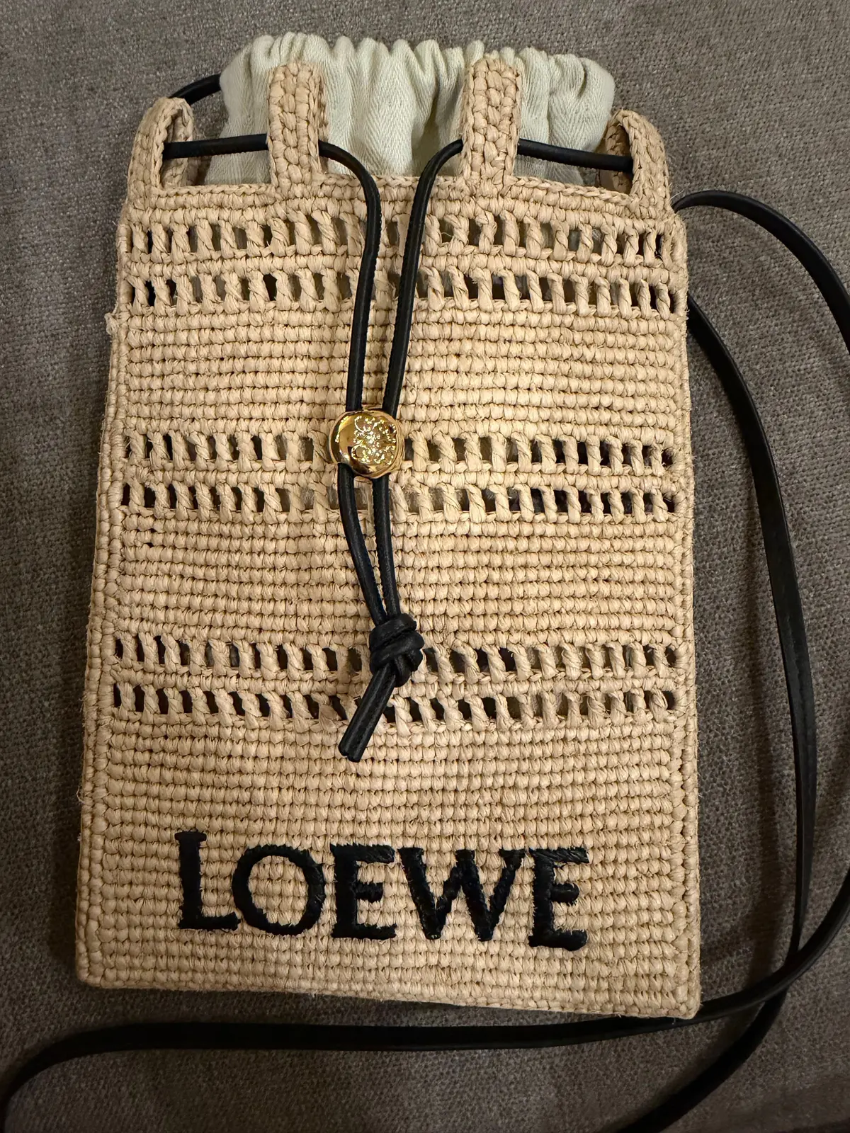ベージュの編みかごバッグで、LOEWEの文字が黒で書かれています。黒のストラップと金のチャームが付いています。