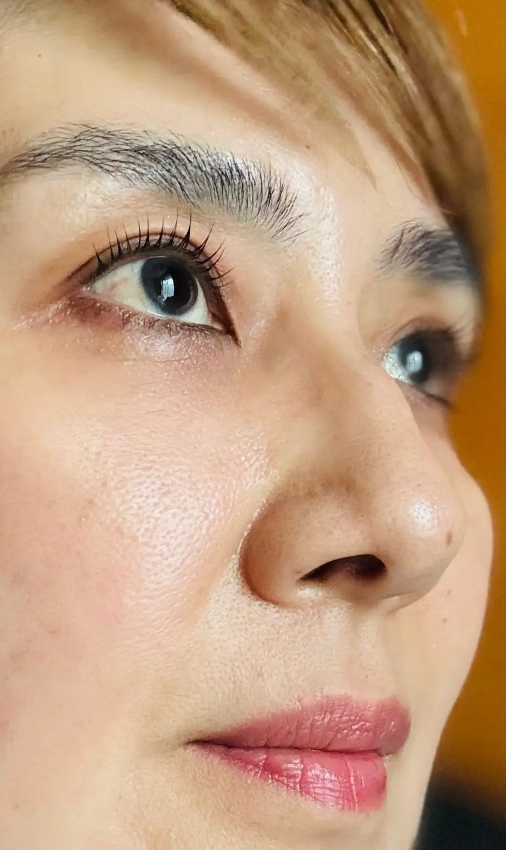 黄色の背景に、女性の顔のアップ。茶色の前髪が額にかかり、明るい色のアイシャドウとリップを施している。右耳には金色のドロップ型のピアスが光る。