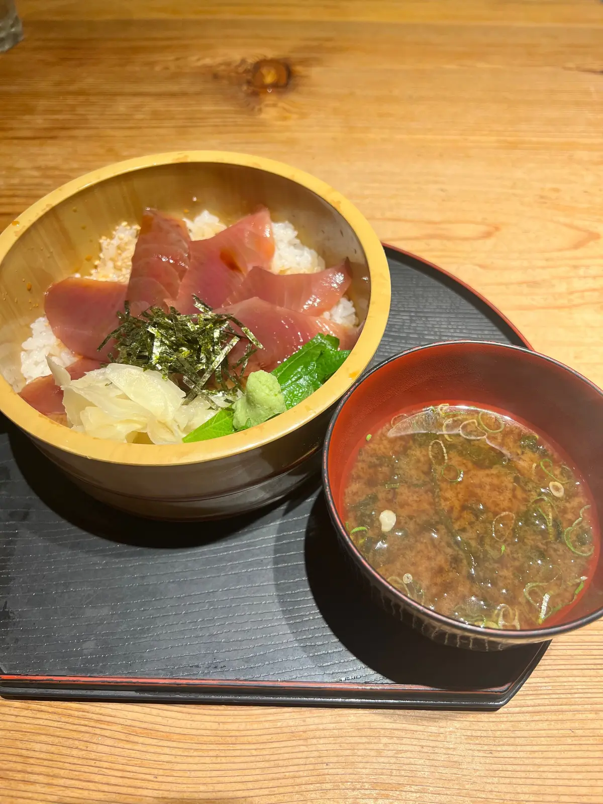 てこね寿司。木製の漆器に盛り付けられた、マグロ丼と味噌汁のセット。マグロ丼には、赤身のマグロと白髪ねぎ、海苔が乗っている。味噌汁には豆腐とわかめ、ネギが入っている。