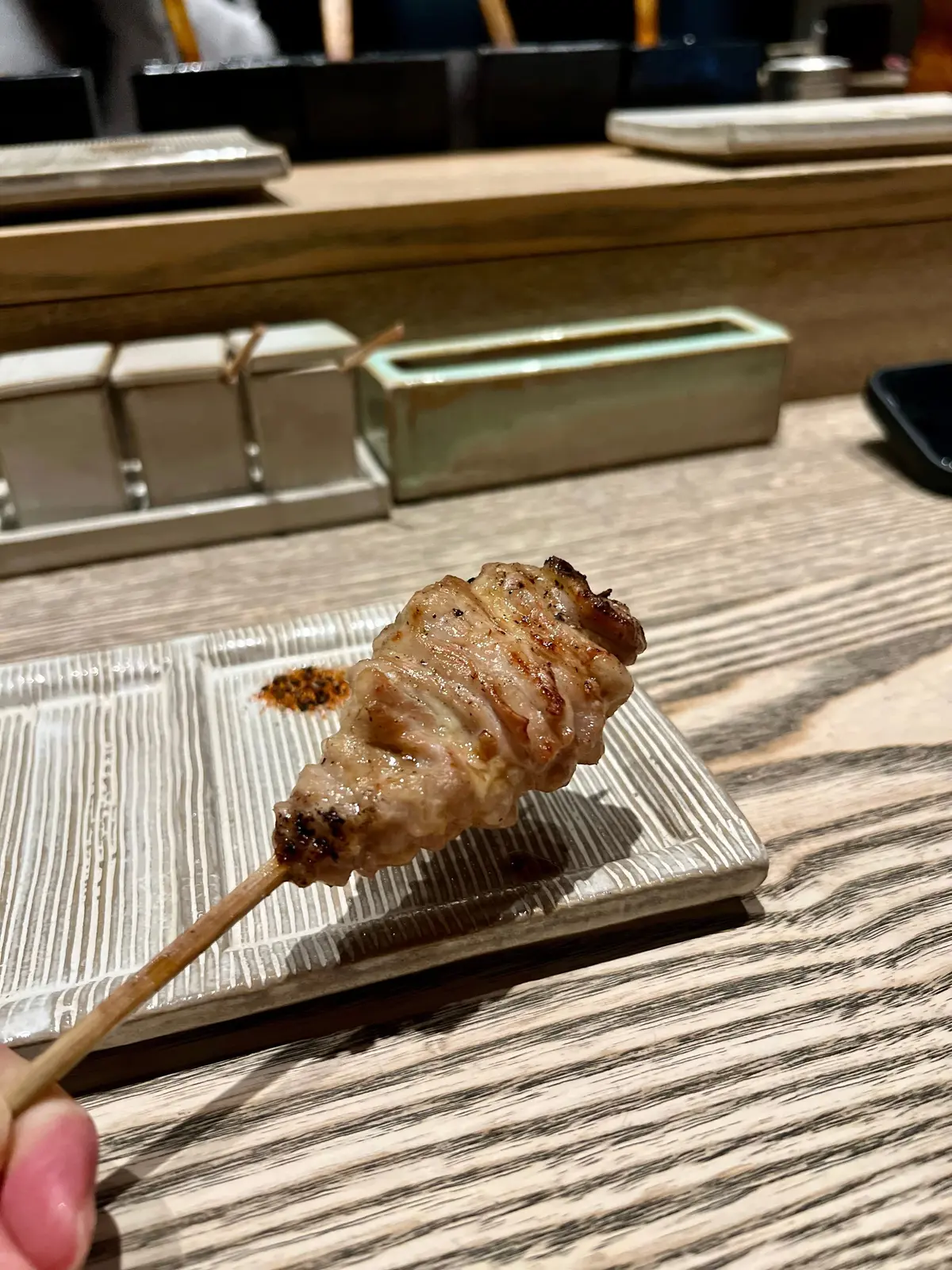 焼き魚の串焼きが木製の串に刺さり、焼き色が付いた表面が木製のプレートに置かれている。プレートには少量の焼き色が付着している。
