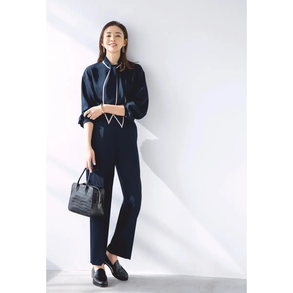 白のパイピングが施されたタイがついたネイビーブラウスにネイビーパンツを合わせたコーディネート　モデル・SHIHO