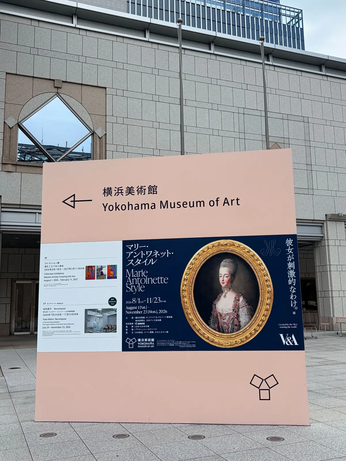 横浜美術館の正面玄関。グレーの建物で、入り口付近に「Marie Antoinette Style」の展覧会ポスターが掲示されている。ポスター中央には、18世紀風の肖像画が額装されて配置。右側にはV&Aのロゴマーク。