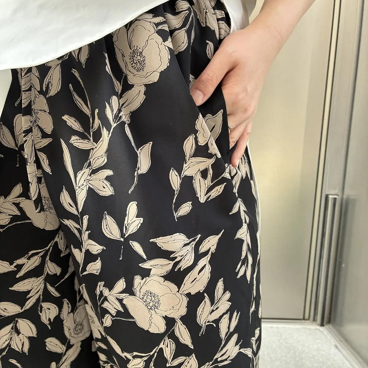 黒のスカートに花と葉の模様が施された女性の手がポケットに置かれている