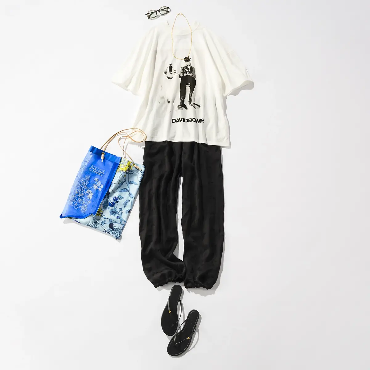 白のTシャツにデビッド・ボウイのグラフィック、黒のワイドパンツ、黒のサンダル、青と白のショルダーバッグ、首にチェーンと眼鏡が配置されたファッションコーデ