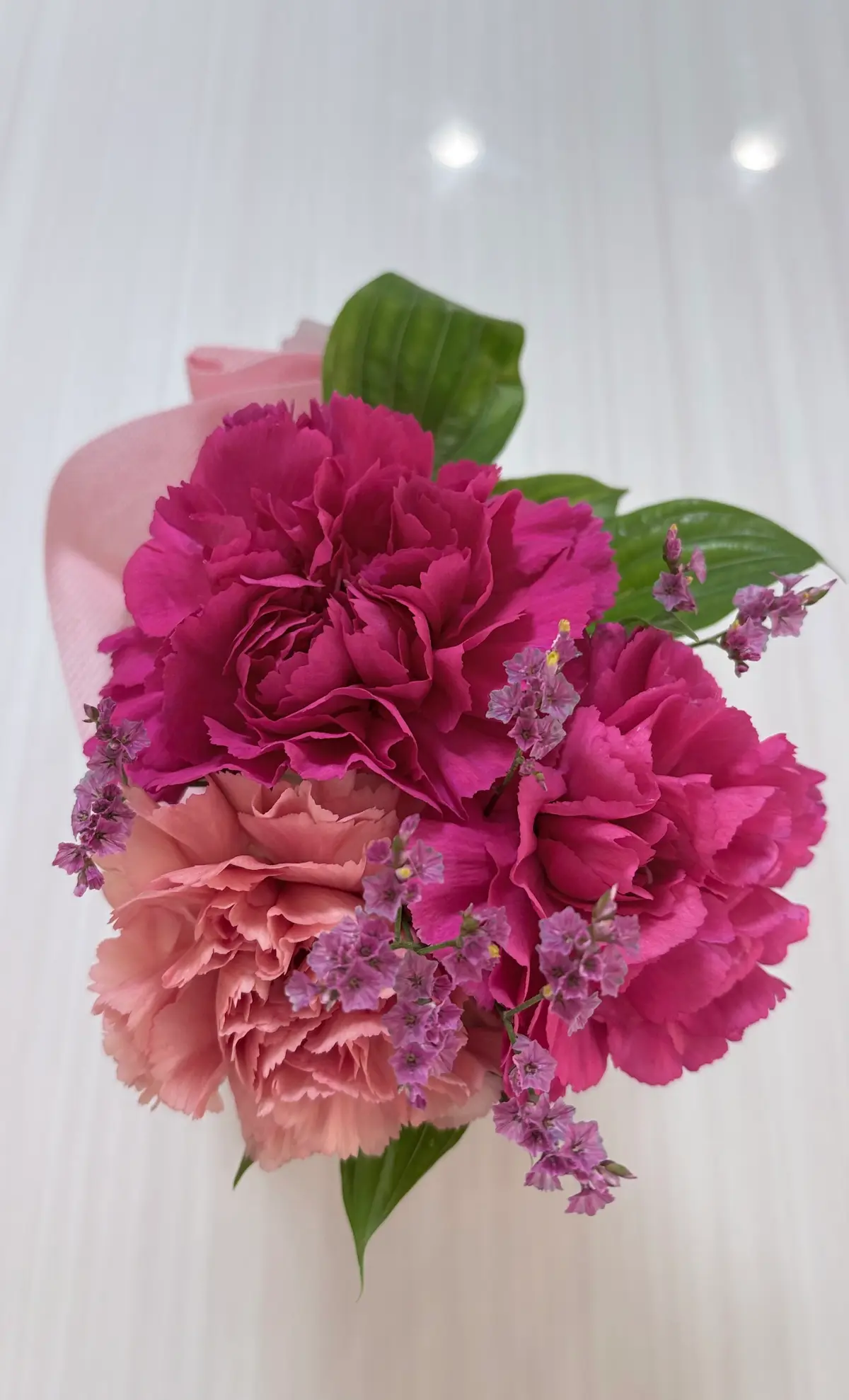 ピンクとラベンダーの花が緑の葉とともに白い背景に配置された花束