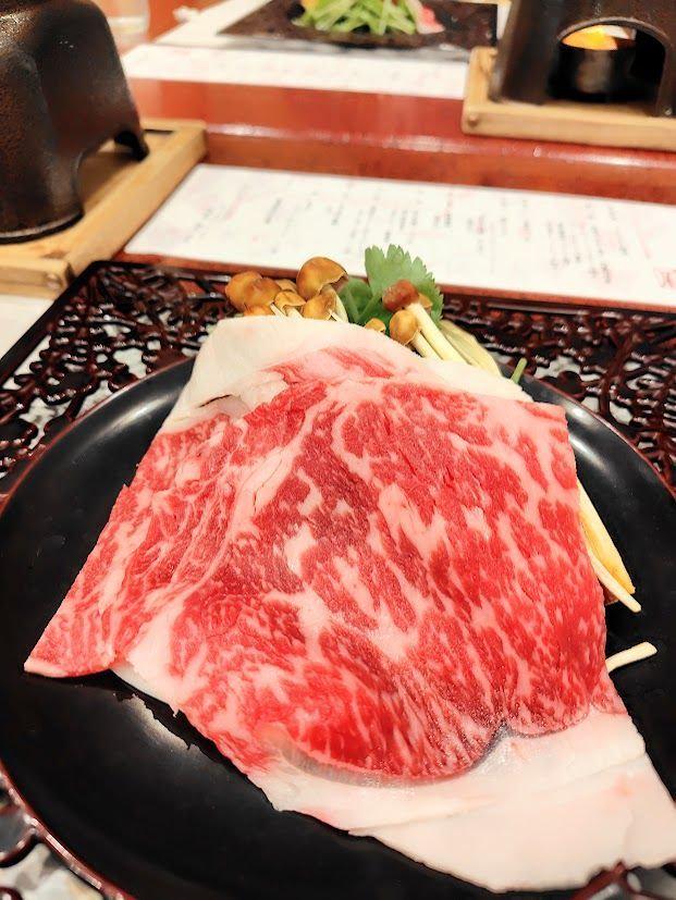 赤身が豊富な和牛のステーキが黒い皿に盛り付けられ、しいたけとネギが添えられている