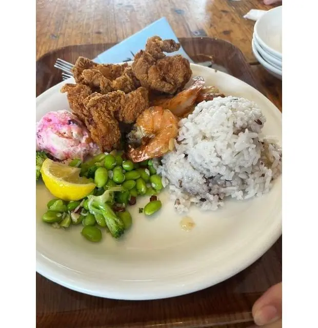 フライドチキン、エビ、米、豆腐、ブロッコリー、レモンなどの料理が盛り付けられた白い皿