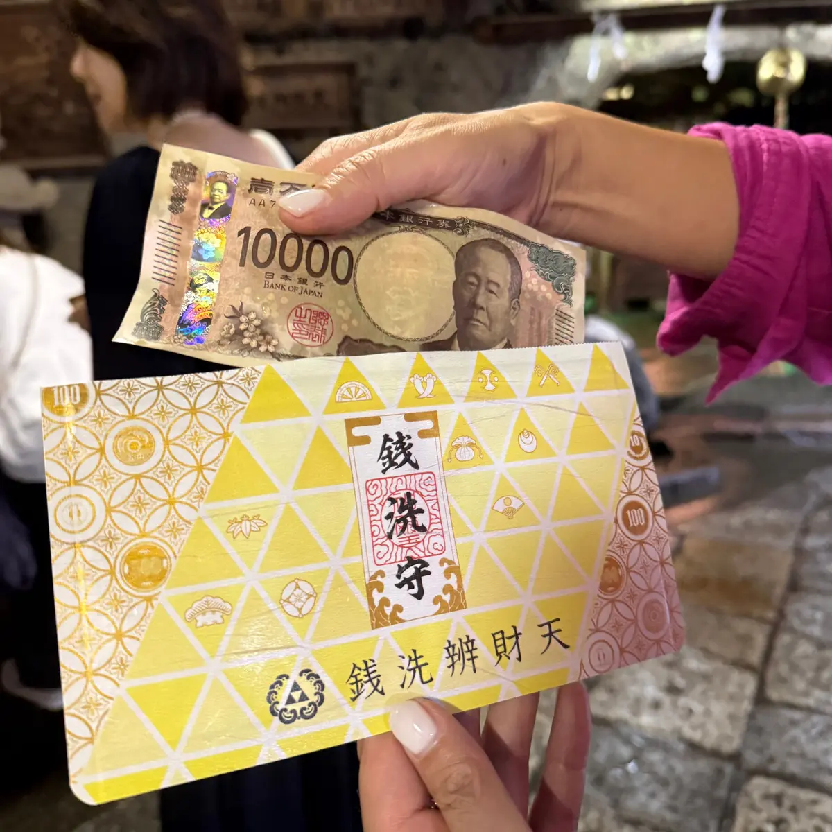 手は日本の10,000円紙幣と100円硬貨を保持、背景は混雑した店内