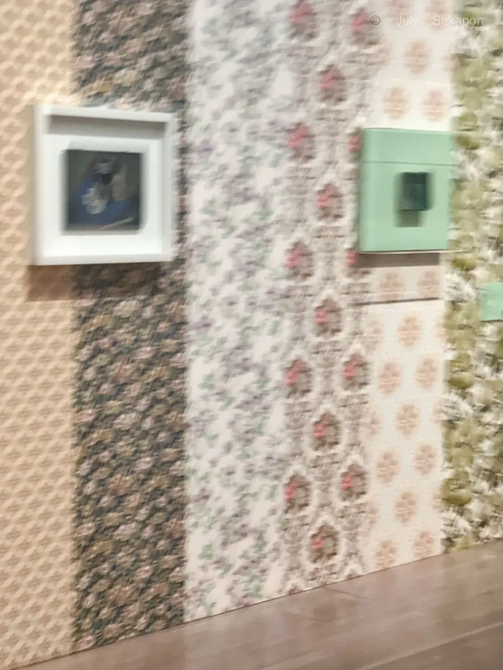 花模様の壁紙に額装された絵画と緑の箱が並ぶ部屋の角