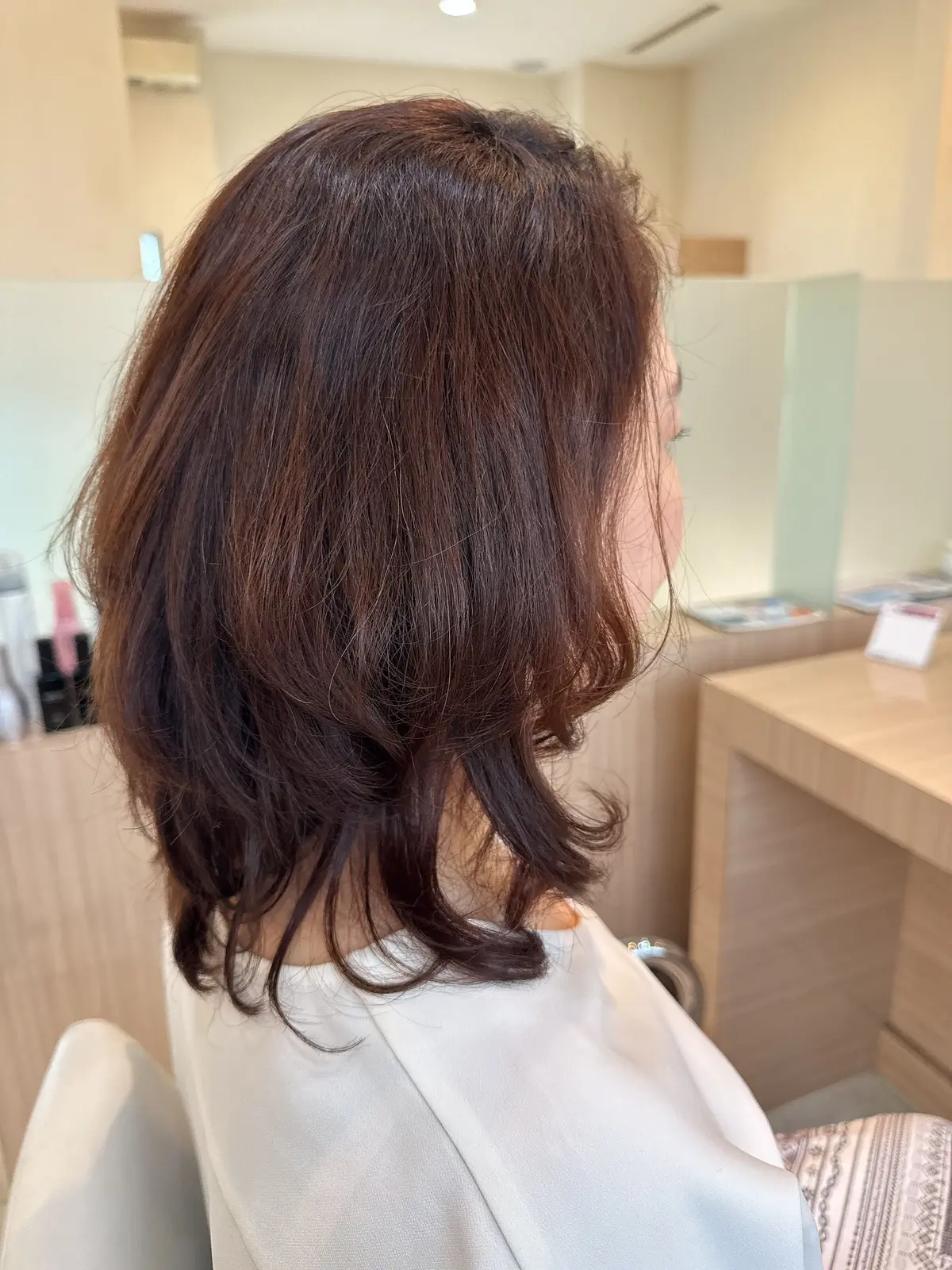 肩くらいの長さのダークブラウンの髪をブロンドのシャツを着た女性。髪はゆるくカールがかかっており、後ろ姿が写っている。