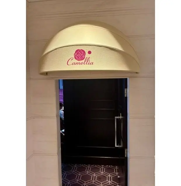 オフホワイトのアーチ状看板に、ピンク色の花と「Camellia」のロゴマークがある。ドアの奥は暗く、床には幾何学模様のカーペットが敷かれている。