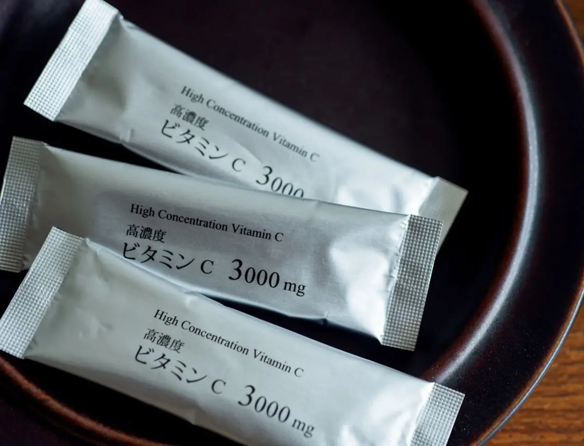 茶色の陶器の器に、白い個包装のビタミンCサプリメント3袋が置かれている。各袋には「High Concentration Vitamin C 3000 mg」と日本語で「高濃度 ビタミンC 3000」と記載されている。