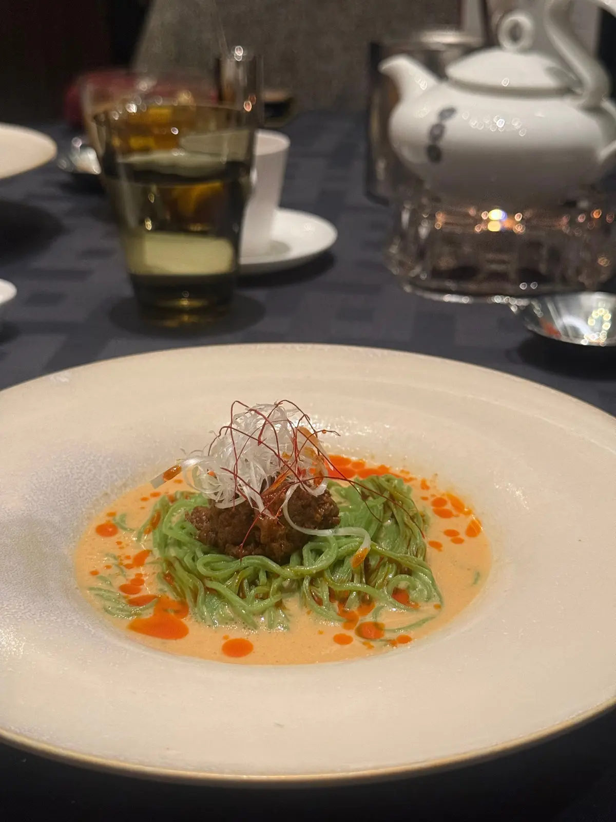 白い皿に緑の細麺と肉の盛り合わせ、赤いソースと細い糸のような装飾がトッピングされた料理