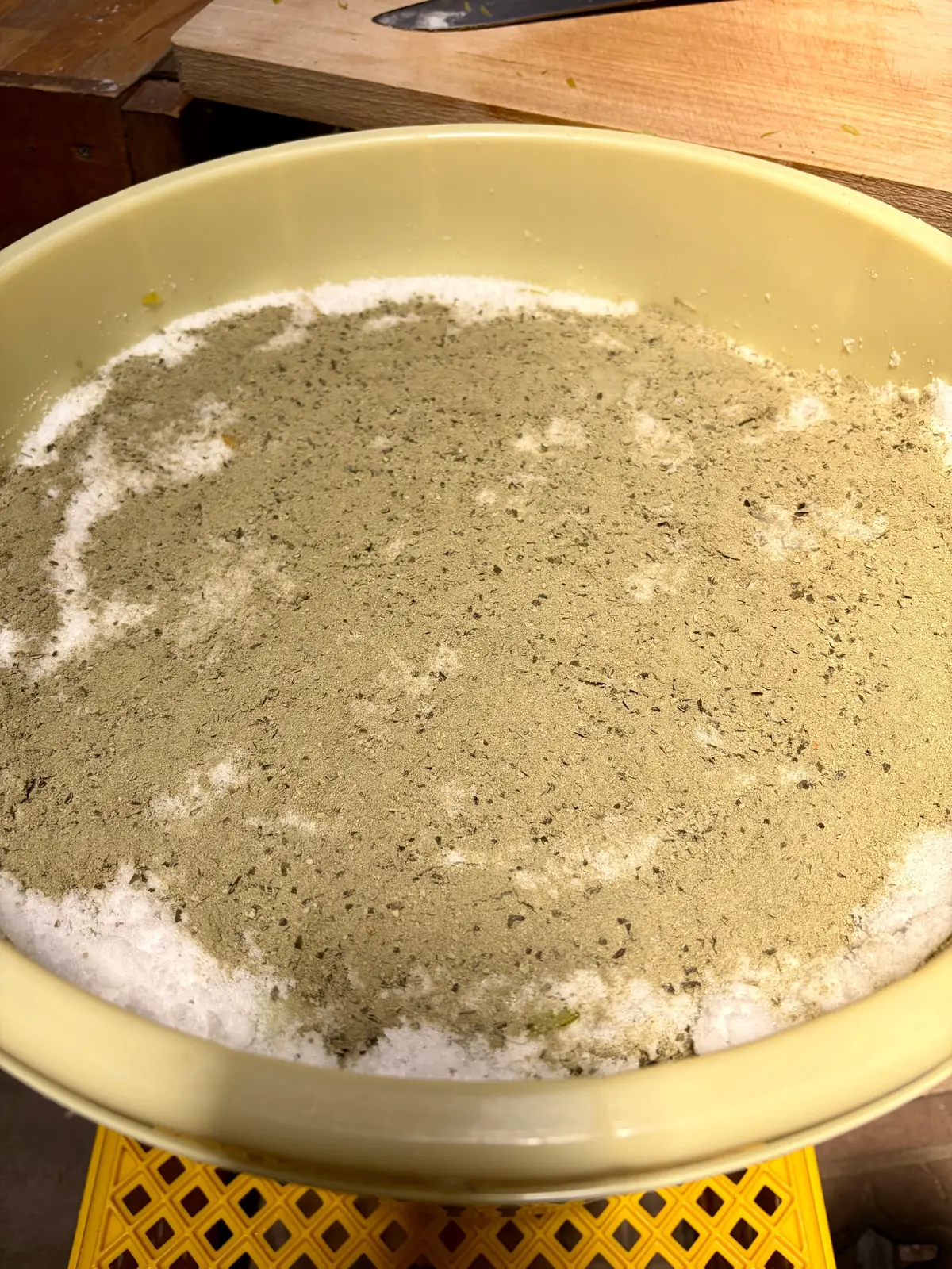 ベージュのボウルに小麦粉と茶色い粉が混ざり、表面に白い粉が少し散らばっている