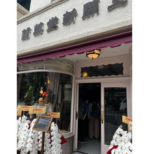 白い建物の店頭、紫のテント屋根付きの入口、窓には花とディスプレイ、店名「黄金茶屋」、白い花が並ぶ