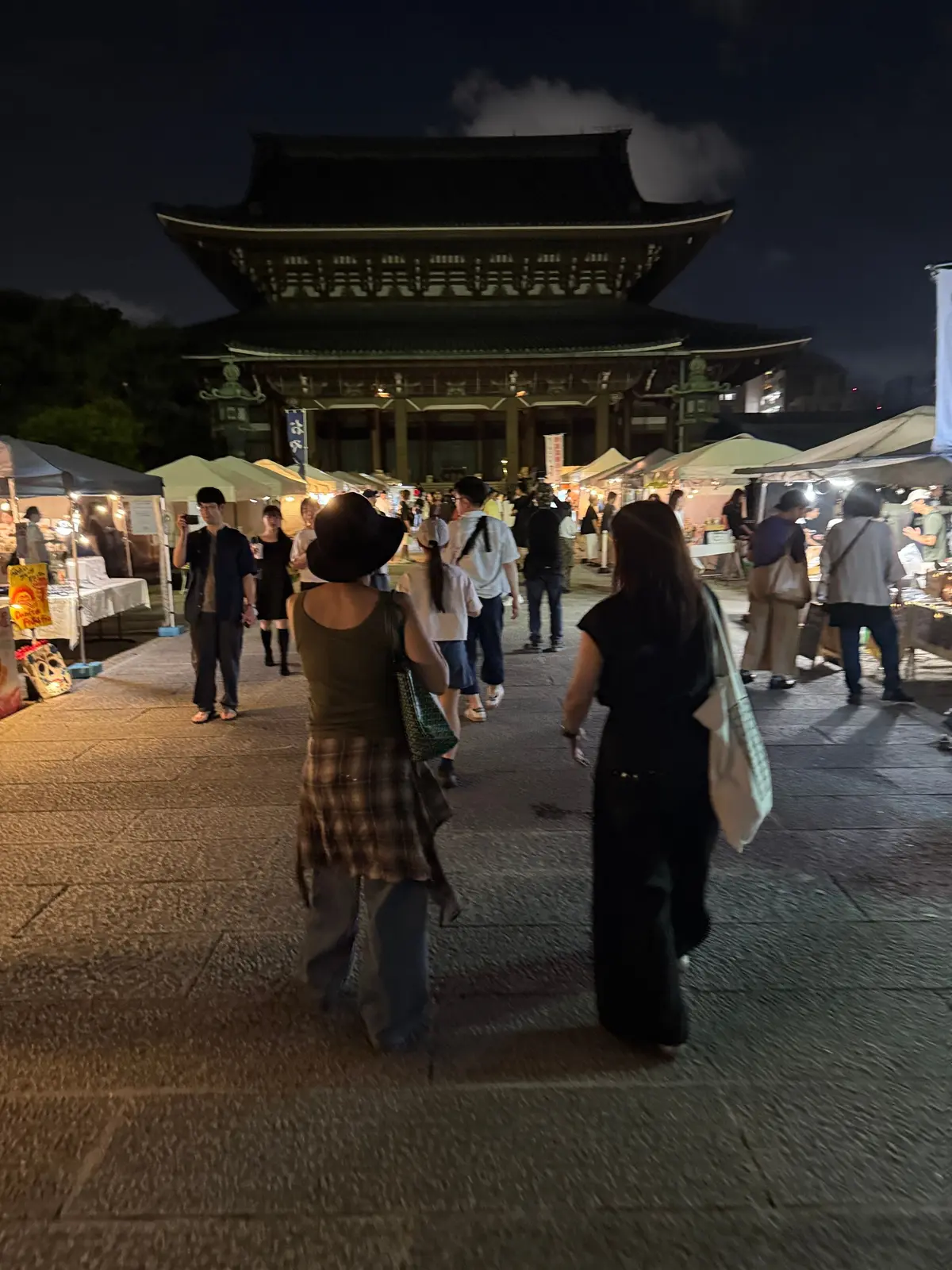 夜の市場で人々が歩く様子。背景には、緑色の照明で照らされた伝統的な韓国建築の建物が見える。手前には、テントが並び、多くの人が集まっている。