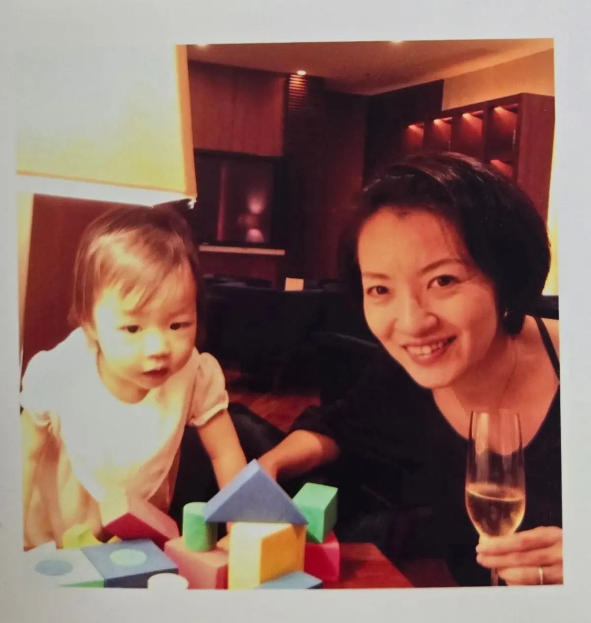 赤ん坊が積み木で遊ぶ様子、母親がグラスを持って微笑む